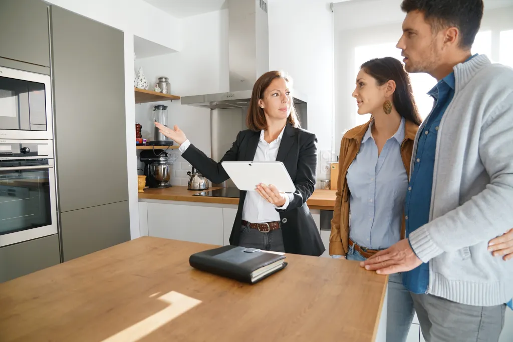 A real estate agent showing a kitchen with stainless steel appliances to potential buyers.