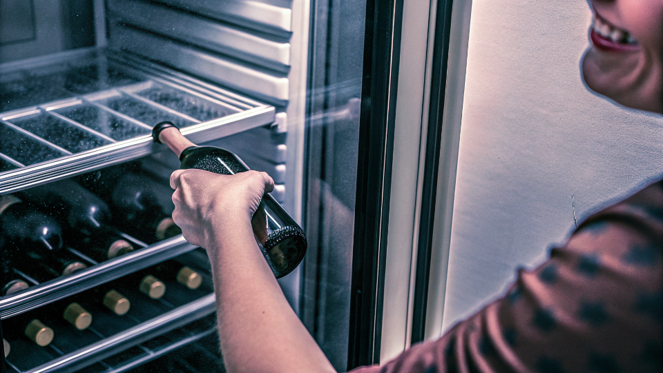 A person smiling as they take a bottle of wine from a cooler