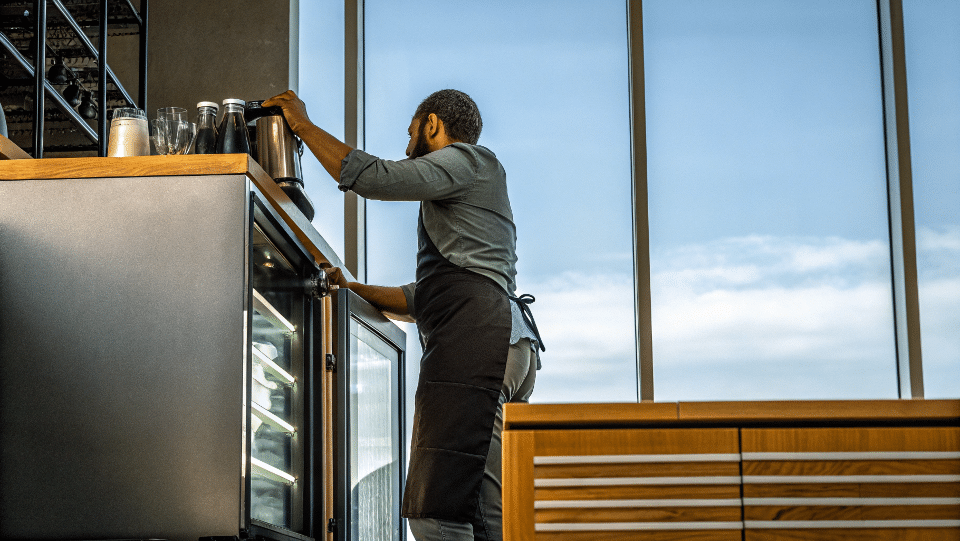 A barista easily reaching into an undercounter cooler next to an espresso machine