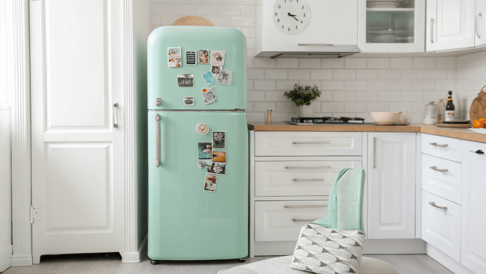 A mint green retro fridge styled with a few curated magnets in a white kitchen