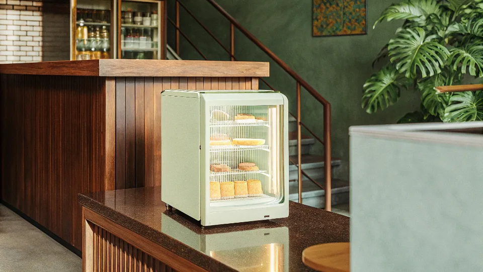 A stylish cream-colored countertop display fridge in a modern coffee shop.
